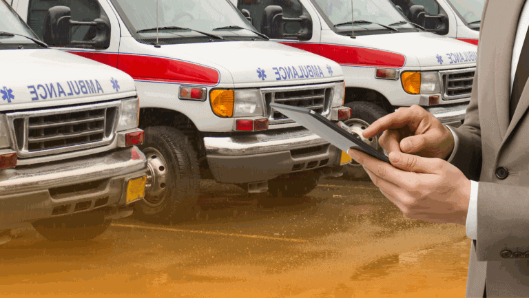 Person in business attire using a tablet in front of a row of parked ambulances, overseeing their fleet safety program.